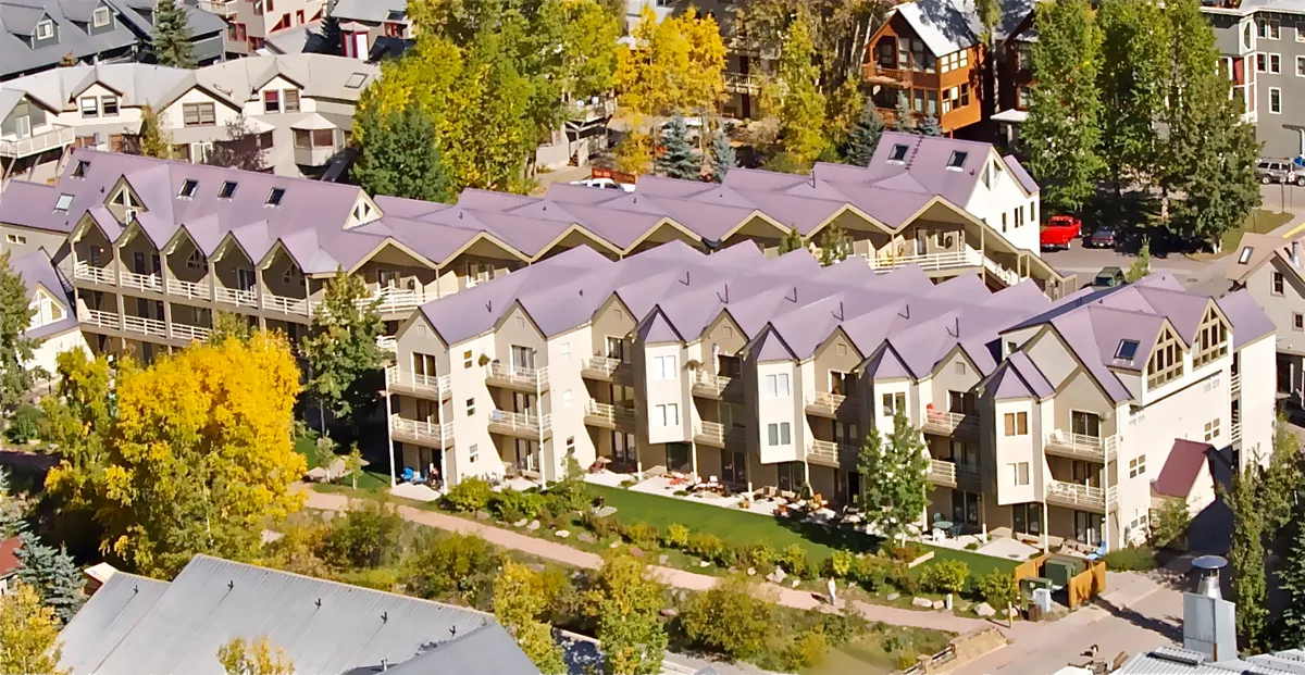 Rows of charming townhouses surrounded by vibrant greenery and decorative balconies. Groups gather for outdoor barbecues and family picnics in the sunshine, showcasing the community atmosphere. The setting is perfect for evening events and socializing with neighbors and friends.