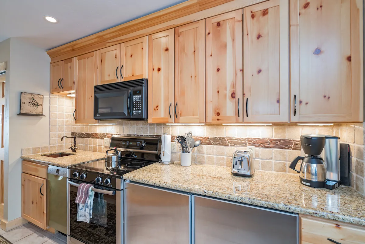 A spacious, modern kitchen featuring a polished granite countertop, rich wooden cabinetry, and gleaming stainless steel appliances. The counter is set for meal preparation, with utensils and coffee-making essentials at hand, evoking an atmosphere ready for lively family breakfasts or evening feasts.