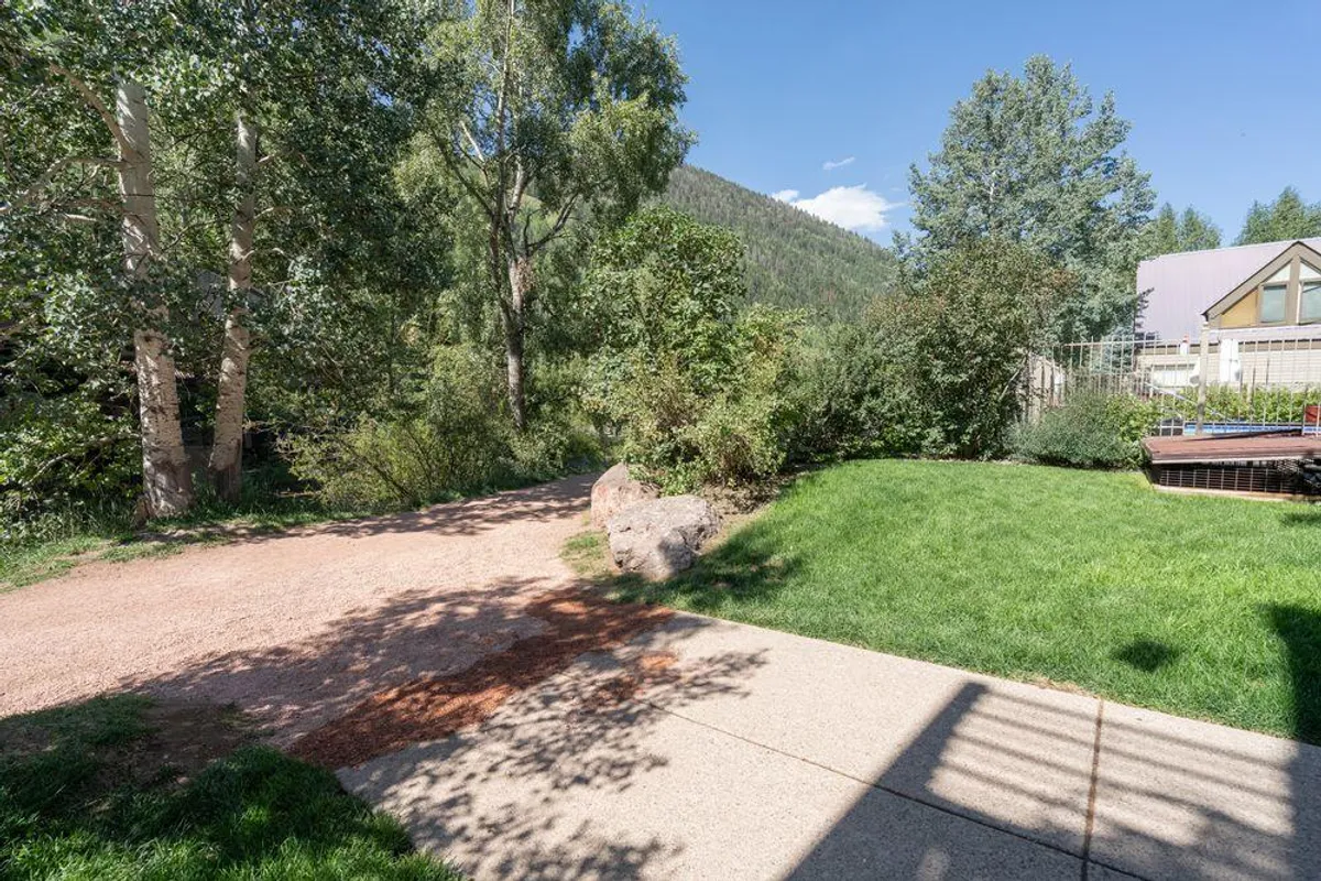 A grassy area with a clear, stroller-friendly pathway winding through tall trees, bathed in soft sunlight. The scene is tranquil and inviting, suggesting morning walks or relaxed family outings. The approachable landscape hints at accessibility for all ages.