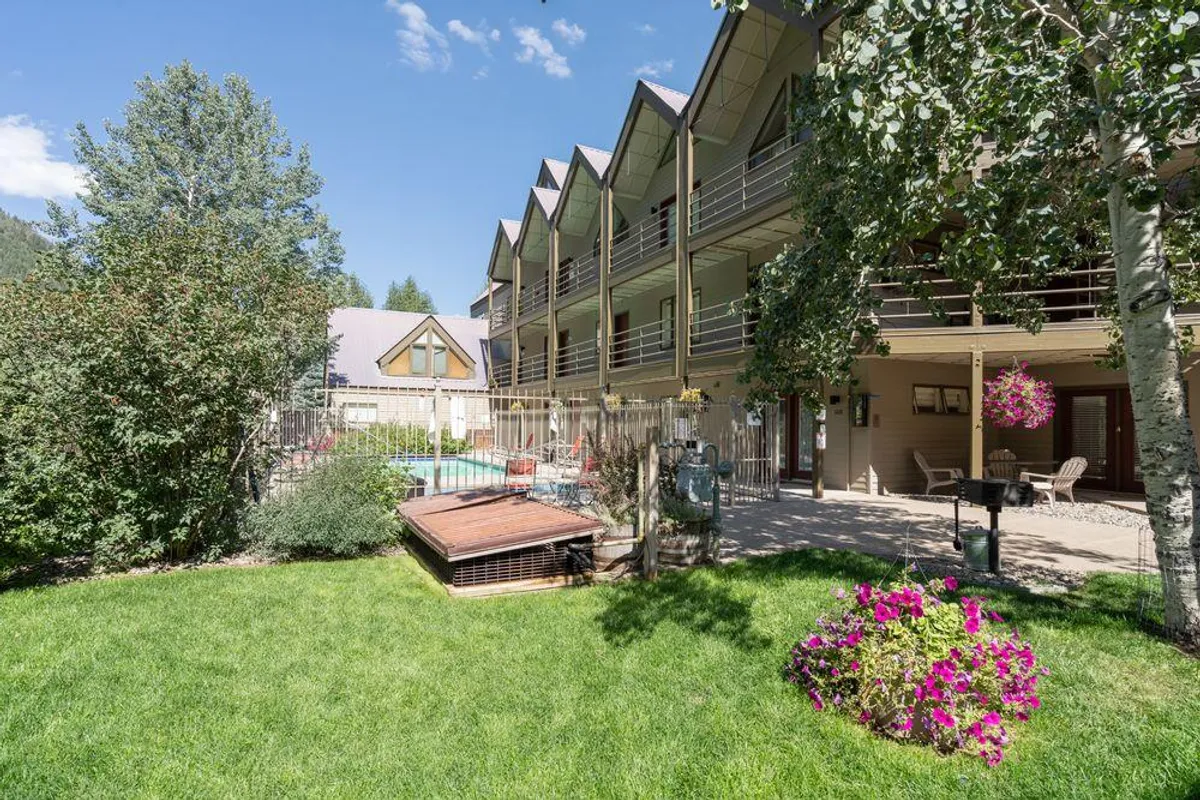 A cheerful outdoor pool area surrounded by colorful flower beds and the balconies of the Viking Lodge building. Sunlight sparkles on the heated saltwater pool, with lounging and gathering spaces for socializing and relaxation. Visible features include the pool itself, sunbathing spots, and proximity to the building's communal amenities.